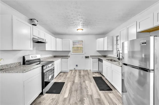 a kitchen with granite countertop a refrigerator a sink dishwasher a stove and white cabinets with wooden floor