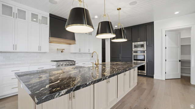 1682 North 1950 W Street, Unit 9 Provo, UT 84604 - Photo 19 of 84 Kitchen featuring a large island with a patterned countertop, brass-toned fixtures, white shaker-style cabinetry, dark cabinetry surrounding built-in appliances, and light wood-finish flooring