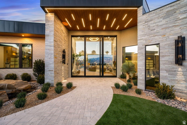 2867 East Granite Way St. George, UT 84790 - Photo 67 of 69 Modern exterior design featuring natural stone accents, a wood-paneled entry ceiling with recessed lighting, full-light entry doors, a paver pathway, and curated landscaping