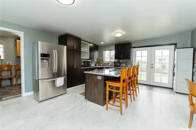 a kitchen with stainless steel appliances kitchen island granite countertop a refrigerator a stove a sink a dining table and chairs with wooden floor