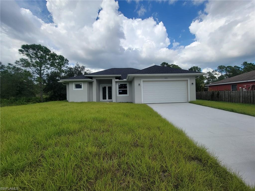 1900 West 16th Street Lehigh Acres, FL 33972 - Photo 2 of 21 a view of a white house in front of a big yard with plants and large trees