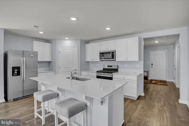 a kitchen with stainless steel appliances a stove a sink a refrigerator and white cabinets with wooden floor