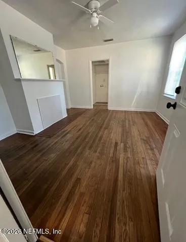 a view of an empty room with wooden floor and a window