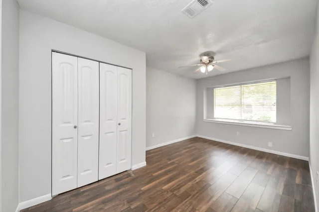 an empty room with wooden floor ceiling fan and windows
