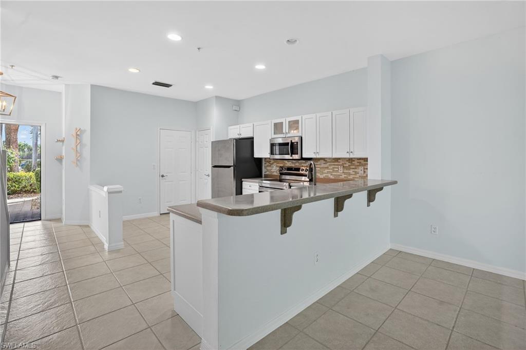15995 Caldera Lane, Unit 69 Naples, FL 34110 - Photo 5 of 27 Kitchen with a peninsula, a kitchen bar, light tile patterned floors, white cabinets, and stainless steel appliances