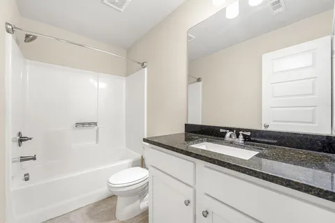 a bathroom with a granite countertop sink a toilet a mirror and bathtub