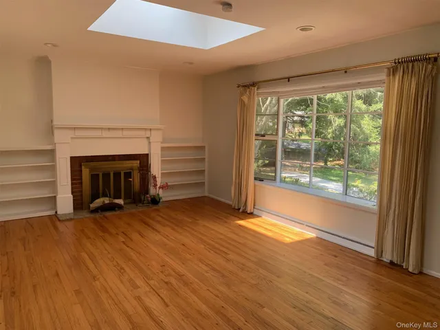 a view of an empty room with wooden floor fireplace and a window