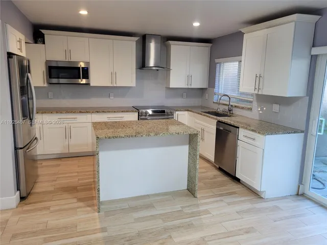 a kitchen with stainless steel appliances granite countertop a stove a sink a refrigerator and white cabinets with wooden floor