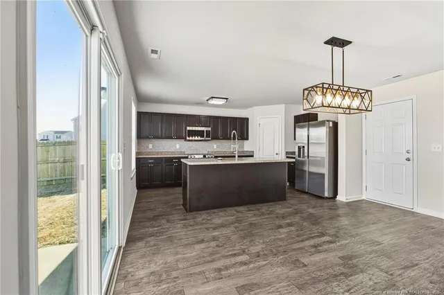 a kitchen with stainless steel appliances granite countertop a refrigerator a sink dishwasher a stove and a dining table with wooden floor