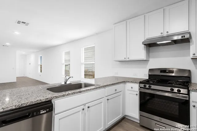 a kitchen with granite countertop a sink dishwasher stove and white cabinets