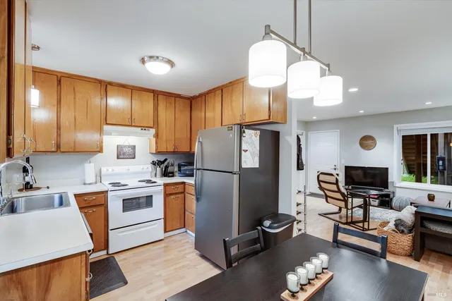 a kitchen with stainless steel appliances granite countertop a refrigerator a stove a sink dishwasher a dining table and chairs with wooden floor