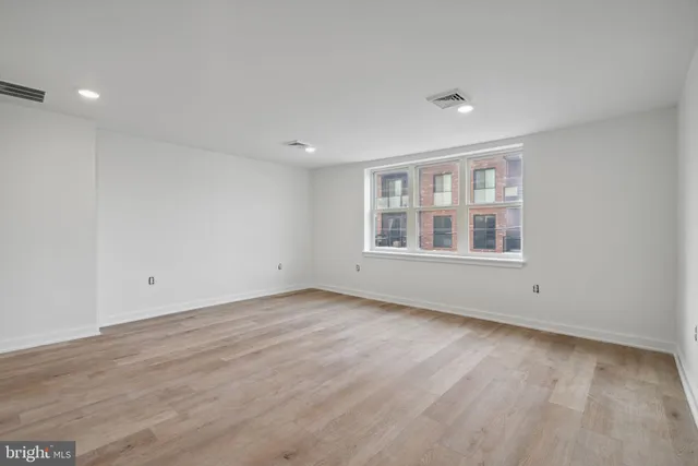 a view of an empty room with wooden floor and window
