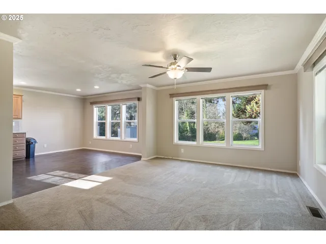 a view of an empty room with chandelier fan and wooden floor
