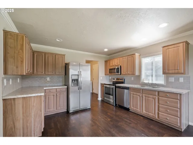 a kitchen with stainless steel appliances granite countertop white cabinets a refrigerator a sink a stove a microwave and wooden floors