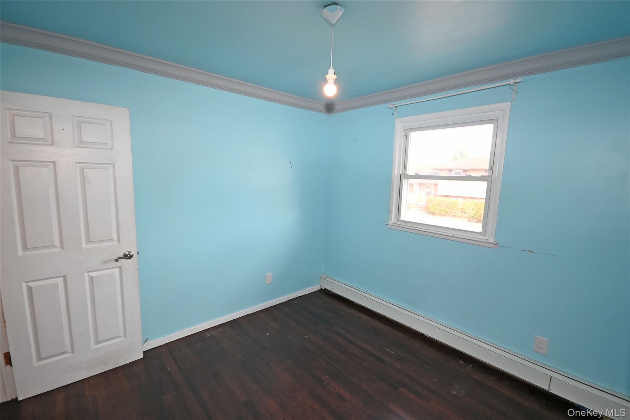 89 Osborne Road West Hempstead, NY 11552 - Photo 8 of 50 Empty room featuring a baseboard radiator, crown molding, and dark wood-style flooring