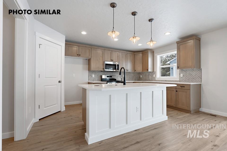 1644 Haystack Emmett, ID 83617 - Photo 10 of 33 Kitchen featuring a white island with shiplap-style detailing, wood-finish flooring, light-toned cabinetry, a herringbone tile backsplash, and three pendant lights