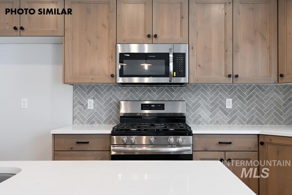 1644 Haystack Emmett, ID 83617 - Photo 11 of 33 Kitchen featuring light wood cabinetry with dark hardware, stainless steel appliances, a grey herringbone tile backsplash, and white countertops