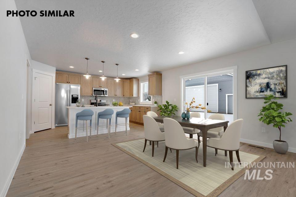 1644 Haystack Emmett, ID 83617 - Photo 5 of 33 Open-concept living space featuring wood-finish flooring, a kitchen island with pendant lighting, stainless steel appliances, light wood cabinetry, and a dining area with sliding glass doors