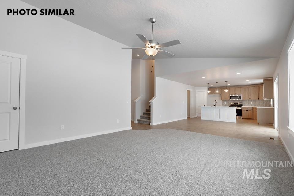 1644 Haystack Emmett, ID 83617 - Photo 7 of 33 Open-concept living area featuring a ceiling fan with integrated lighting, soft gray carpeting, and a bright kitchen with light wood-finish cabinetry, a central island, and stainless steel appliances