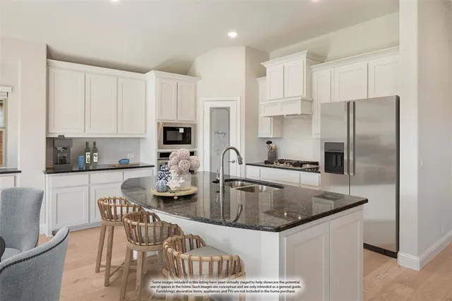 a kitchen with stainless steel appliances granite countertop a dining table chairs refrigerator and sink