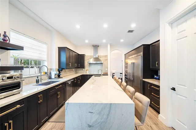 a kitchen with stainless steel appliances kitchen island granite countertop a dining table chairs stove refrigerator and cabinets