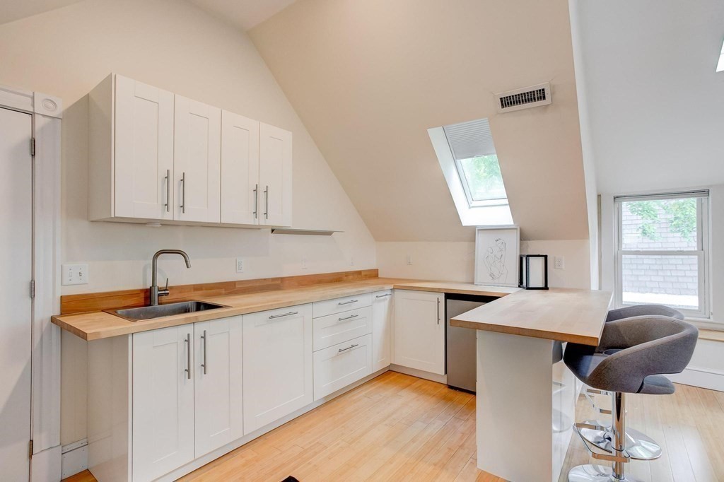 59 Creighton Street, Unit 2 Cambridge, MA 02140 - Photo 27 of 38 a kitchen with stainless steel appliances granite countertop a sink and white cabinets with wooden floor