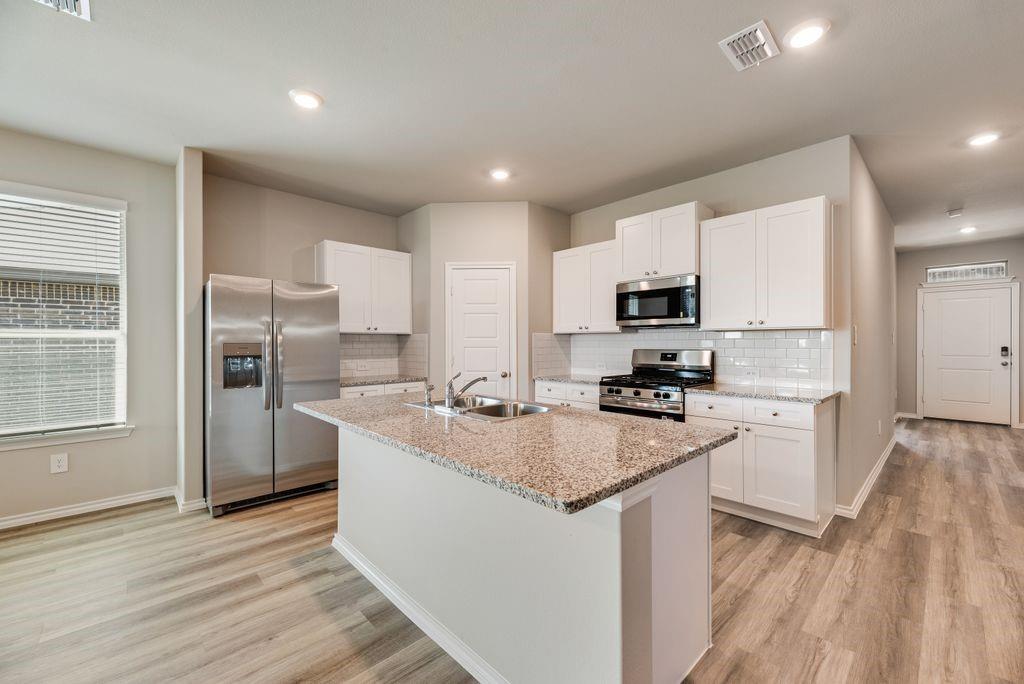 752 Rubicon Road Justin, TX 76247 - Photo 8 of 19 Kitchen featuring a central island with a granite countertop and integrated double basin sink, stainless steel appliances, white shaker cabinetry, subway tile backsplash, and wood-finish flooring