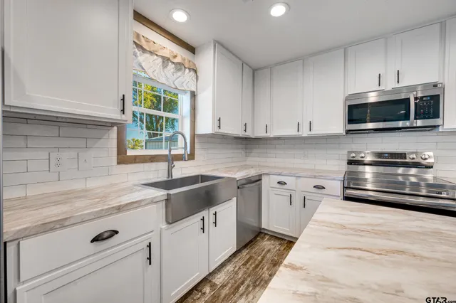 a kitchen with granite countertop white cabinets stainless steel appliances and a window
