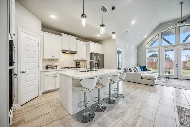 a kitchen with stainless steel appliances kitchen island granite countertop a stove a sink a refrigerator and white cabinets with wooden floor