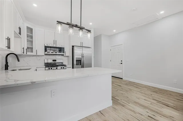a view of a kitchen with stainless steel appliances a center island wooden floor and a chandelier
