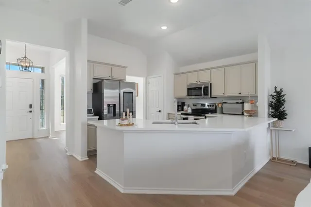 a view of kitchen with stainless steel appliances granite countertop a refrigerator a stove top oven a sink a refrigerator and white cabinets with wooden floor