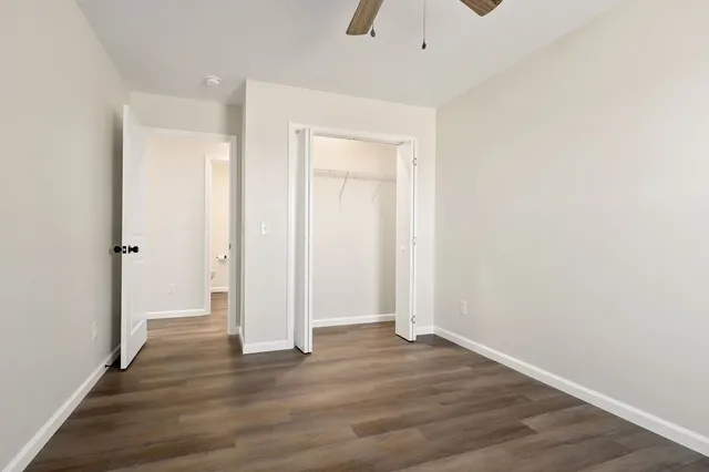 an empty room with wooden floor fan and windows