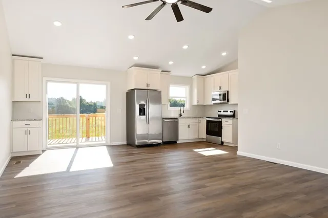 a large white kitchen with stainless steel appliances granite countertop a stove a sink a refrigerator and white cabinets with wooden floor