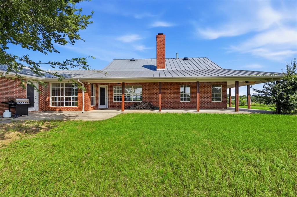 12190 Bell Road Pilot Point, TX 76258 - Photo 38 of 39 Brick exterior with a metal roof, featuring a covered patio and a red brick chimney