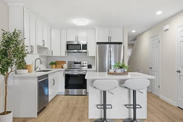 a kitchen with stainless steel appliances a sink stove refrigerator and white cabinets with wooden floor