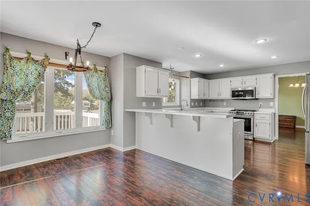 a kitchen with stainless steel appliances granite countertop a stove top oven a sink a refrigerator white cabinets and wooden floor next to a window
