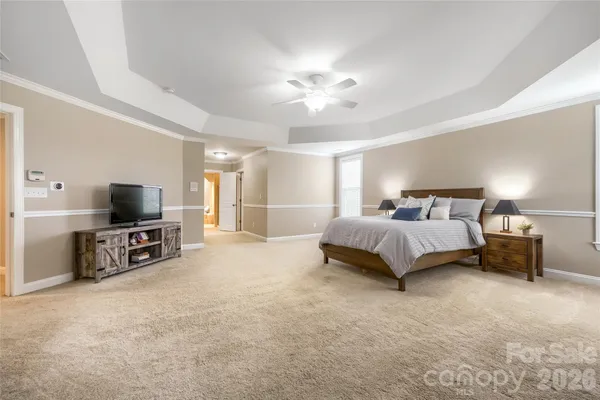 a spacious bedroom with a bed and a flat tv screen on dresser