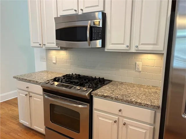 a kitchen with stainless steel appliances granite countertop white cabinets and a stove top oven