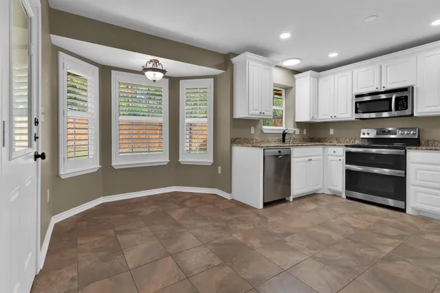 a kitchen with stainless steel appliances granite countertop a stove top oven a sink a refrigerator and white cabinets