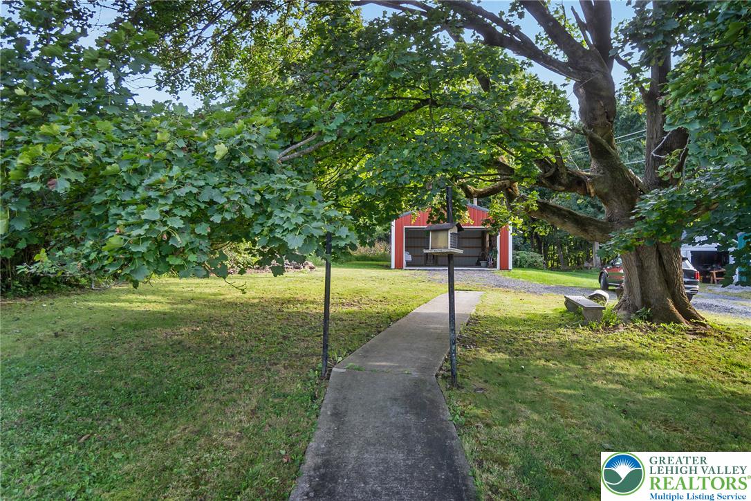 506 Richmond Road Bangor, PA 18013 - Photo 4 of 43 A concrete walkway leads through mature trees toward a detached garage on the grassy lawn.