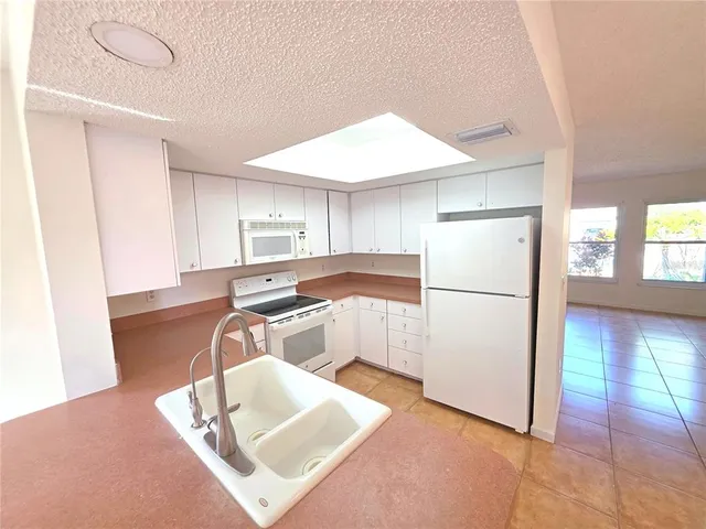 a kitchen with stainless steel appliances granite countertop a refrigerator a sink a stove and white cabinets with wooden floor