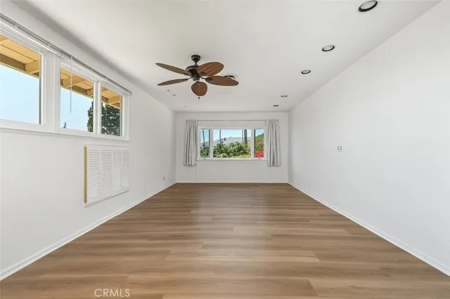 an empty room with wooden floor ceiling fan and windows