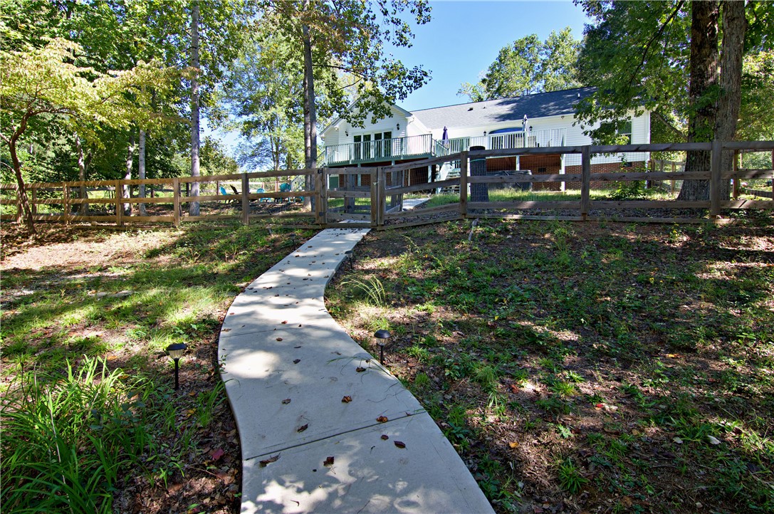 206 Petty Road Seneca, SC 29672 - Photo 38 of 49 A curved concrete walkway leads through a fenced yard toward the rear deck.