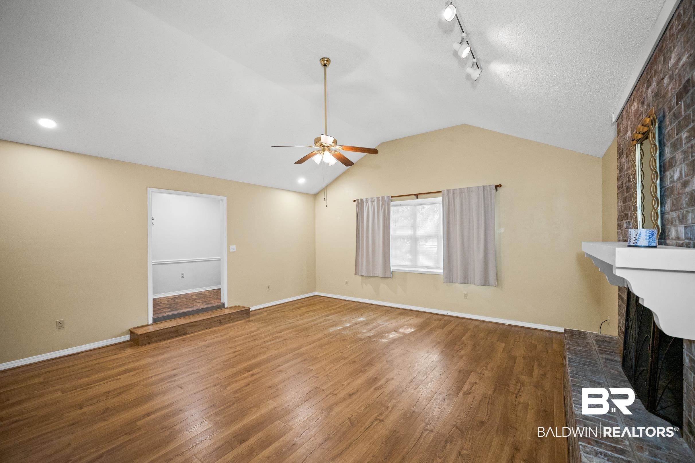 123 Dunbar Loop Daphne, AL 36526 - Photo 3 of 33 Unfurnished living room with lofted ceiling, hardwood / wood-style flooring, a fireplace, track lighting, and ceiling fan