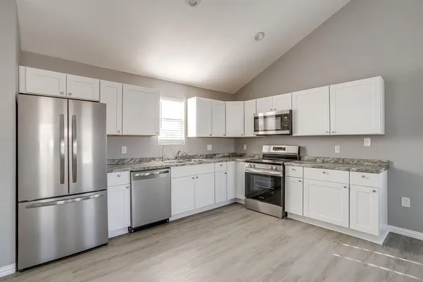 a kitchen with stainless steel appliances granite countertop a stove top oven a refrigerator and white cabinets