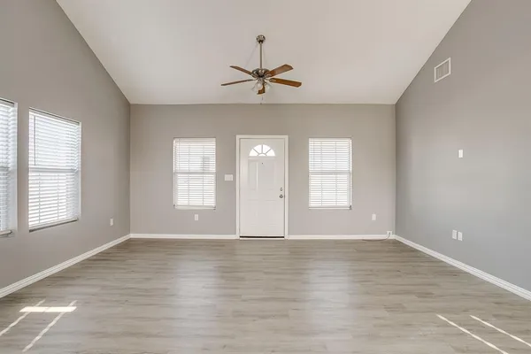 an empty room with wooden floor chandelier fan and windows