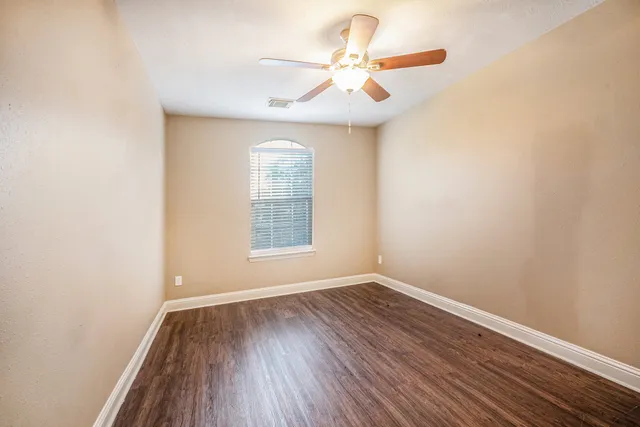 an empty room with wooden floor fan and windows
