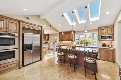 a kitchen with stainless steel appliances granite countertop a refrigerator a stove a sink a dining table and chairs with wooden floor