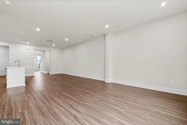 a view of an empty room with wooden floor and a kitchen
