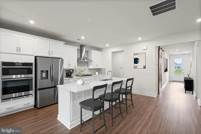 a kitchen with stainless steel appliances a refrigerator a stove a sink dishwasher with a dining table and wooden floor